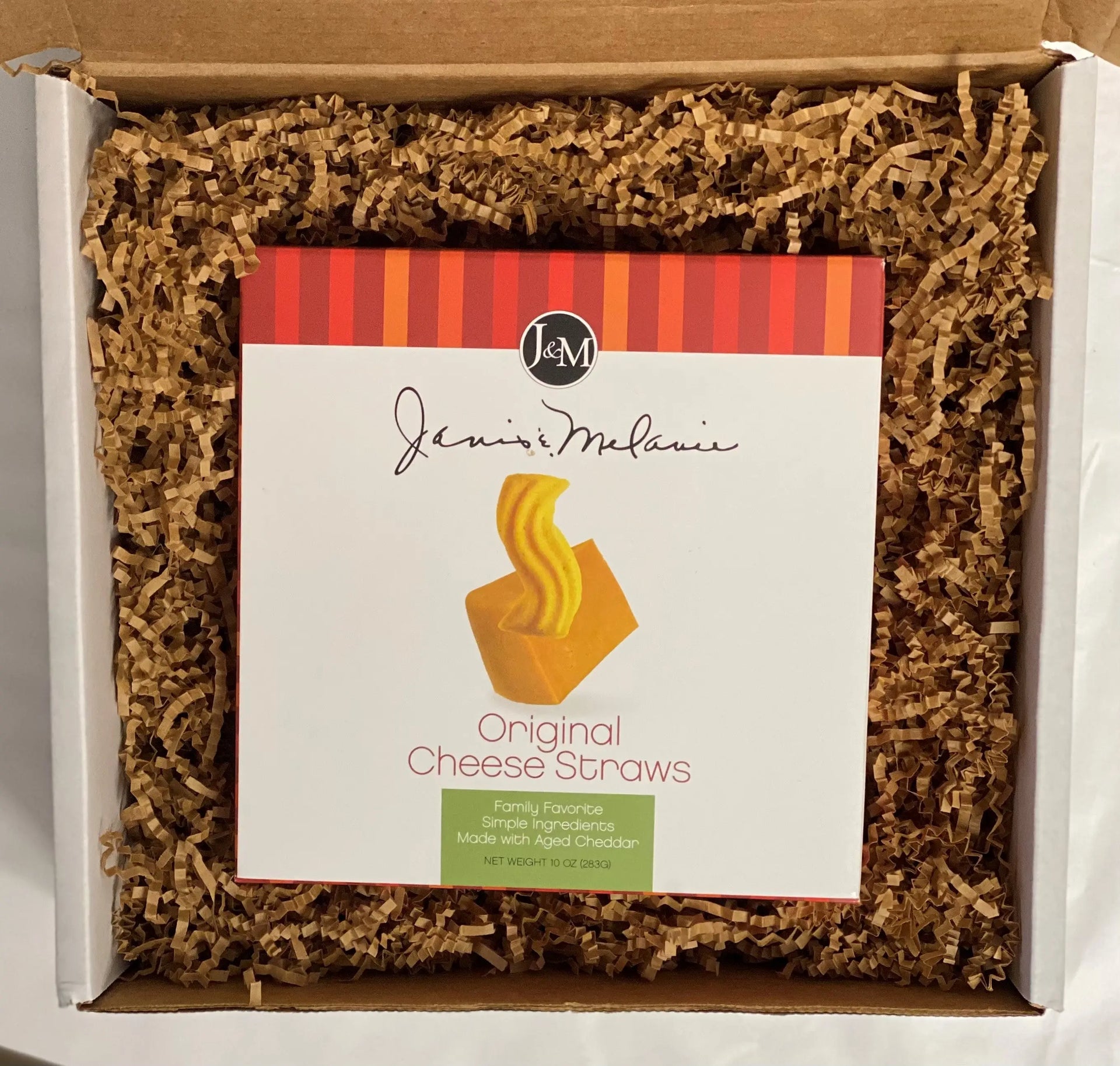 A box of Janis and Melanie Original Cheese Straws, with the product visible inside a Small Food=Love gift box, cushioned with kraft krinkle paper packaging.